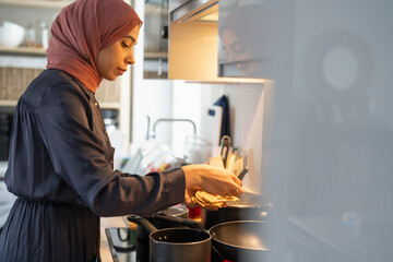 Woman in hijab cooking at home - obrazy, fototapety, plakaty