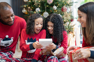 Parents assisting daughters looking at gift in front of Christmas tree