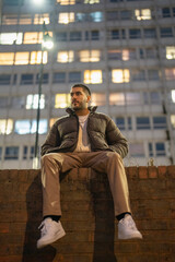 Obraz premium Young man sitting on brick wall at night