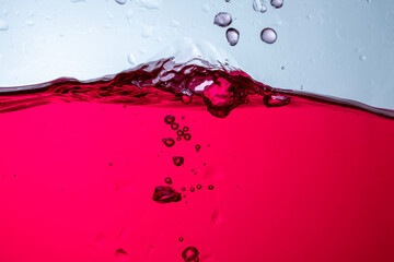 Photograph of juice in a glass jar with water waves. There are bubbles and the background is white.