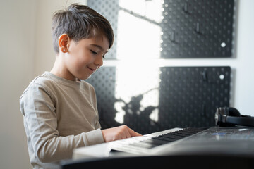 Fototapeta premium Boy (6-7) playing music keyboard at home