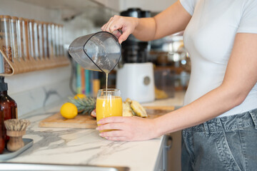 Woman in kitchen, pouring freshly made smoothie, midsection - obrazy, fototapety, plakaty