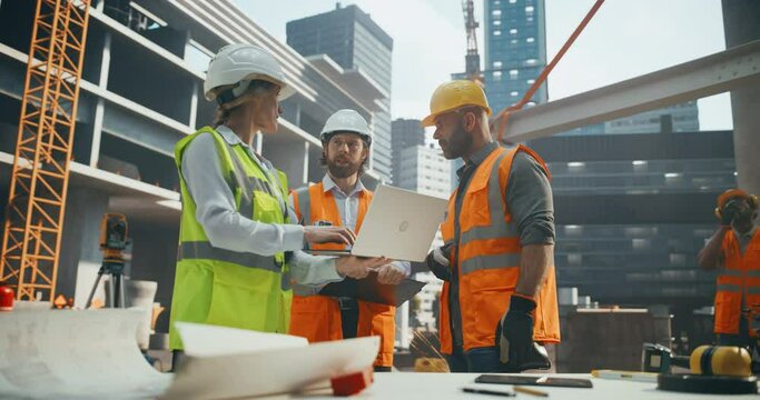 Diverse Female and Male Engineers and Architects Having a Conversation During an Outdoors Meeting at a Building Site Area. Specialists Using Laptop Computer to Discuss Details on a Construction Plan