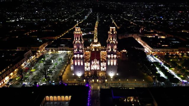 Aerial above the illuminated Morelia Cathedral with the cityscape of Morelia and the streets around