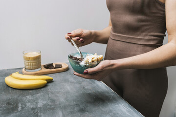Athletic woman in sportswear eating healthy food for breakfast, cereal, granola, muesli, oatmeal with banana, dark chocolate and yogurt in a bowl