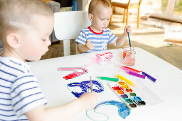Two little brothers in striped T-shirts paint the letters ABC. Young children paint with watercolor...
