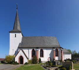 Fototapeta na wymiar Gothic St. Willibrord church with white bell tower and cemetery in Elcherath village, Eifel region in Germany