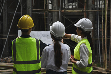 Back view of construction project team holding blueprints while inspecting building at construction site