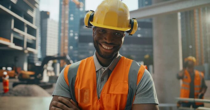 Portrait of Happy Successful Black Construction Worker Standing with Crossed Arms, Posing for Camera, Smiling. Professional Heavy Industry Engineer Wearing Safety Uniform and Protective Hard Hat