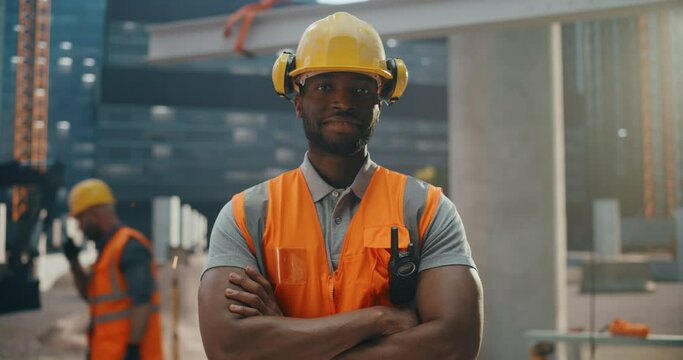 Happy Professional Heavy Industry Engineer Wearing Safety Uniform and Hard Hat on a Residential Building Construction Site. Smiling African American Industrial Site Manager Standing Outdoors