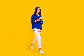 Full body length photo of brunette hair latina lady steps with smartphone buy things in online isolated on yellow color background - obrazy, fototapety, plakaty