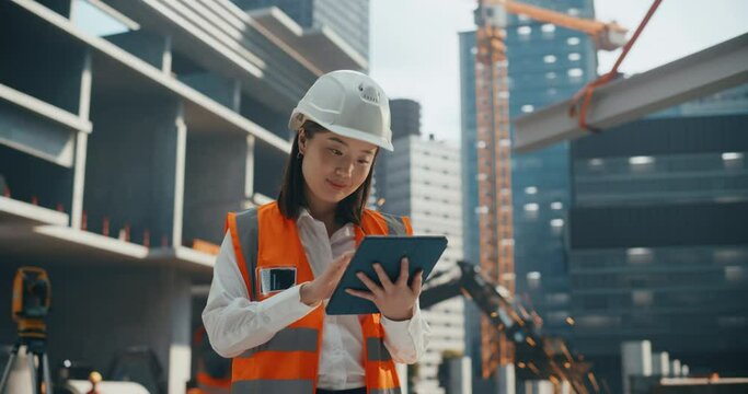 Portrait of a Beautiful Japanese Female Civil Engineer Working on a Tablet at a Construction Site. Young Asian Woman Standing Outdoors, Using Computer for Planning and Developing a Real Estate Project