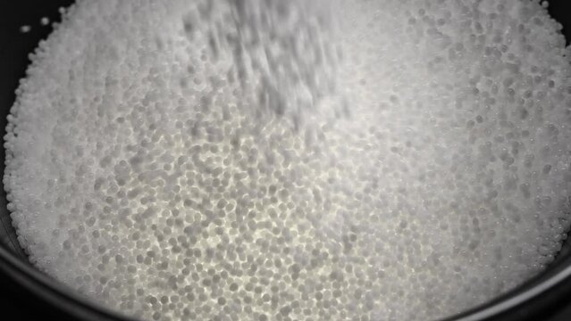 Filling the tank with plastic granules. The process of producing parts from polyethylene compound. White granules are poured into a container.