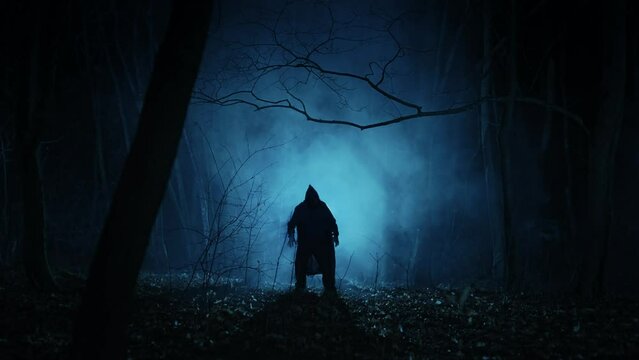 A lonely and frightening figure of a witcher in a dark forest at night. A man in a dark robe with a hood, a creature from the other world.