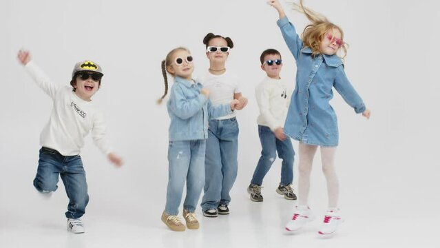 A group of modern, happy children are dancing and having fun on a light isolated background. Concept for clothing advertising, children's shopping and style.