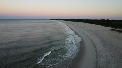Aerial view of a tranquil beach at sunset featuring waves of the ocean crashing against the shore.