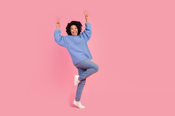 Full size photo of pretty young girl show excited v-sign celebrate wear trendy blue knitted outfit isolated on pink color background
