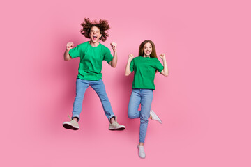Full body size photo of funky couple teenagers jumping wear green t shirt raised fists up crazy fans isolated on pink color background