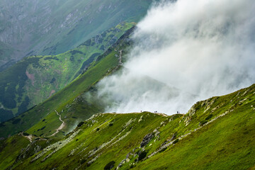 Tourists hiking along the Tatra ridge against a backdrop of billowing clouds on a summer day as seen from Kasprowy Wierch.