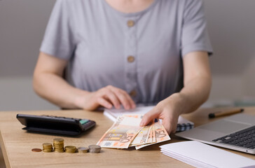 The accountant is holding euro banknotes in his hands. A woman counts money on a calculator and writes down the data in a notebook with white sheets and a laptop. Photo with copy space. High quality