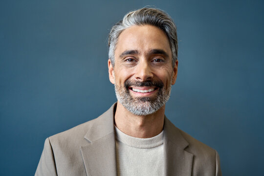 Happy middle aged 50 years old professional business man, smiling older executive ceo manager, mature Indian entrepreneur standing in office work on grey wall looking at camera, headshot portrait.