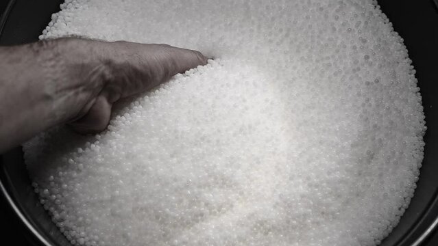 A factory worker checks plastic pellets before they are put into production. White compound in a man's hand. Production