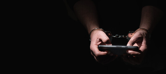 Man's hands tied with metallic handcuffs against dark background as symbol of internet or social media addiction. Copy space.
