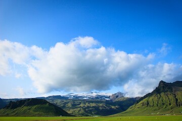 Scenic landscape of a green field in front of a majestic backdrop of mountains