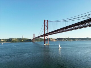 Beautiful shot of a sailboat under a bridge over Tagus River in Lisbon, Portugal