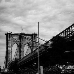 Grayscale of the Brooklyn Bridge against the cloudy sky in New York