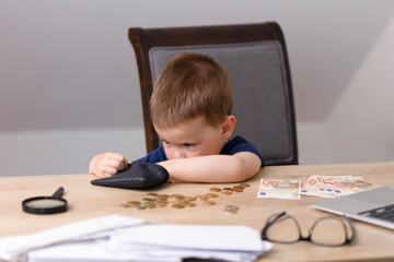 The boy pulls out money from a black wallet and counts coins. On the table next to the boy are...