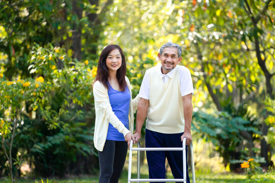 portrait young asian woman caregiver takes disability senior man practice walking with walker in the park