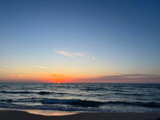 Obraz premium the sun rises over the water on a beach with waves