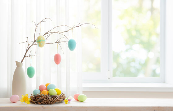 Vase with colorful easter eggs hanging on spring branch and pussy willow nest on table