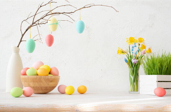 Painted easter eggs on twig in bowl on table with spring flowers and green grass