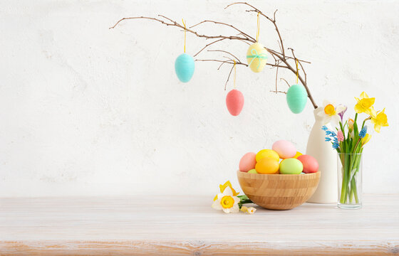 Colorful easter eggs on twig in vase and bowl on table with spring flowers