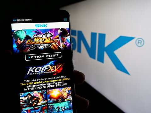 Stuttgart, Germany - 02-06-2024: Person holding cellphone with webpage of Japanese video games company SNK Corporation in front of logo. Focus on center of phone display.