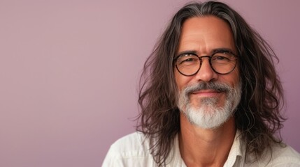 A man with long gray hair and a beard wearing glasses smiling at the camera against a pink background.