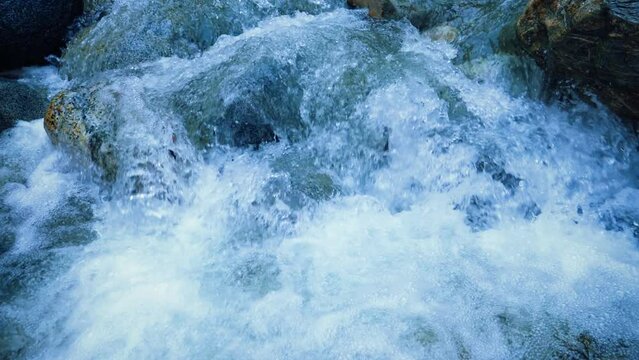 Extreme close up of water falling down the rocks in a river at forest mountain. Blue water. Wild river. Wild rocks. Little waterfall. Slow motion of flowing water in 4k. Wild nature. Water bubbles