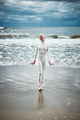 Smiling hairless girl with alopecia in white futuristic suit comes out of cold restless sea on...