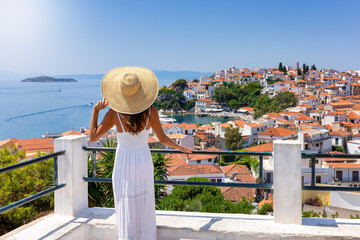 A tourist woman in a white summer dress looks over the beautiful town of Skiathos island, Sporades,...