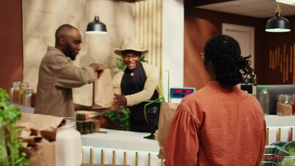 African american vendor weighting produce for regular client at supermarket cash register, using electronic scale to sell locally grown goods. Buyer supporting local farming business. Camera B.
