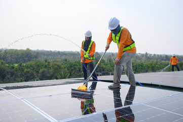 Professional worker cleans solar panels with brush and rinses with water on roof structure of construction factory. Technician uses a mop to clean dirt and dust, green electric power technology
