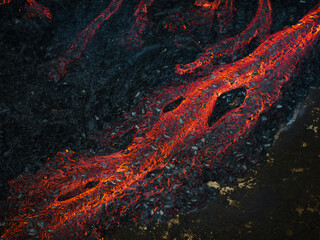 Streams of red hot lava flowing during a volcano eruption, toxic smoke covering the volcanic black...