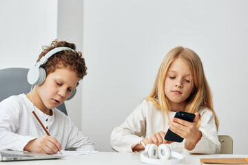 Happy Caucasian children using laptops for elearning at home They are sitting together at a table in their cozy living room, wearing headphones and concentrating on the online lessons