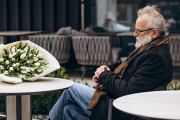 Aged man waiting with bouquet of tulips in a cafe for his date