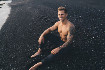 Cheerful young muscular man sitting on sandy beach