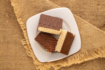 Several sweet chocolate wafers with white saucer on jute cloth, macro, top view.