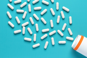 Spilled white pills and plastic bottle on blue background, top view, close-up. Medicine container. Heap of dietary supplements, vitamins. Pharmaceutical medical capsules pattern.