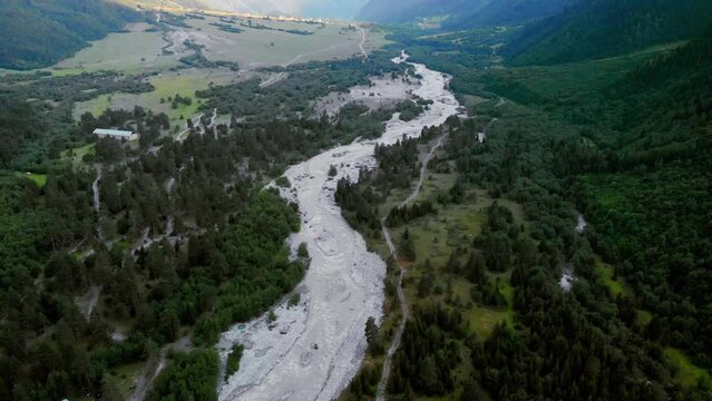 Aerial panorama of the stormy flow of the Dolra River, in the middle of a forest and high Caucasian mountains Ushba, a hiking trail, a tourist route. Mazeri, Georgia